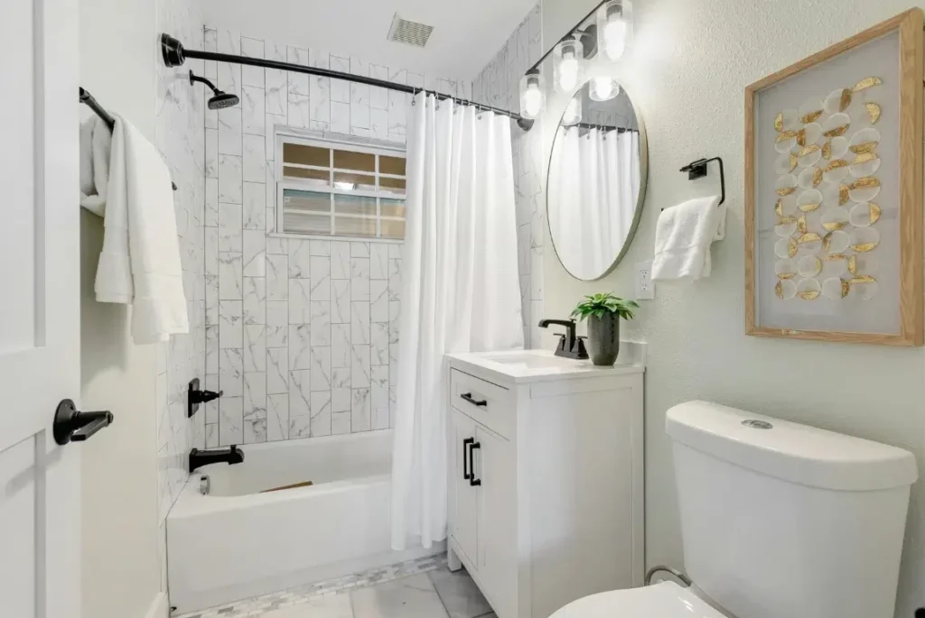 Best Tub to Shower Conversion Oasis Bathroom Boca Raton Modern bathroom featuring a tub and shower combination, white cabinetry, marble tile accents, round mirror, and decorative wall art, showcasing Oasis Bathroom Remodeling Boca Raton's tub-to-shower conversion expertise.