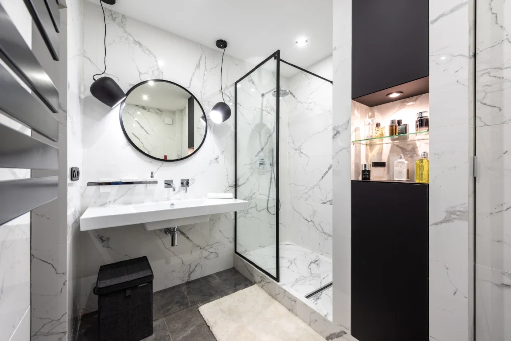 Quality Bathroom Remodel Oasis Bathroom Boca Raton Modern bathroom design featuring a sleek double sink, round mirror, glass shower enclosure, marble walls, and stylish storage for toiletries, exemplifying custom bathroom remodeling solutions in Boca Raton.
