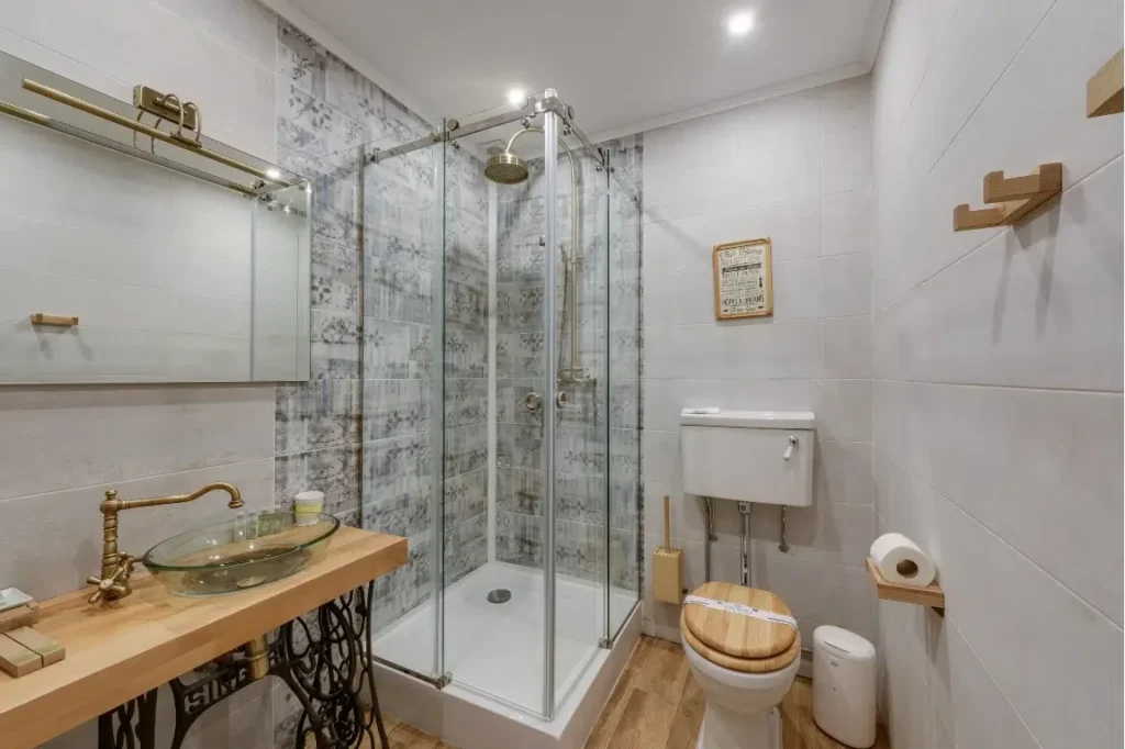 Space Saving Small Bathroom Oasis Bathroom Boca Raton Small modern bathroom featuring a glass shower enclosure, wooden vanity with glass sink, brass fixtures, and stylish tile design, showcasing space-saving elements ideal for compact remodels.