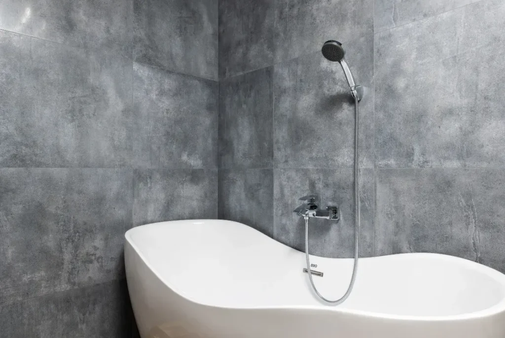 Top-notch Tub to Shower Conversion Oasis Bathroom Boca Raton Modern freestanding tub with handheld showerhead against gray tiled wall, showcasing a stylish bathroom remodel.